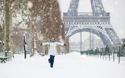 Eine Person steht mit ausgebreiteten Armen im Schnee vor dem Eiffelturm in Paris im Winter.